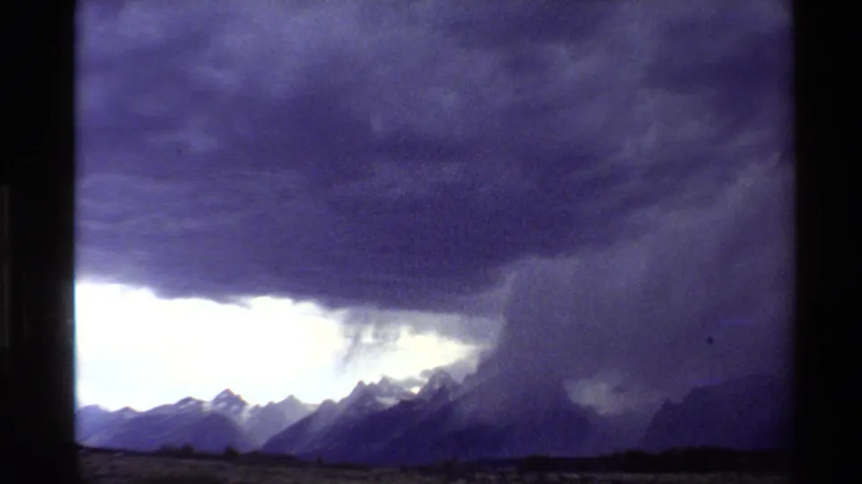 1980 Western U.S. 8mm frame of storm clouds over mountains, with a bright lightning-like streak near the right side of the sky.