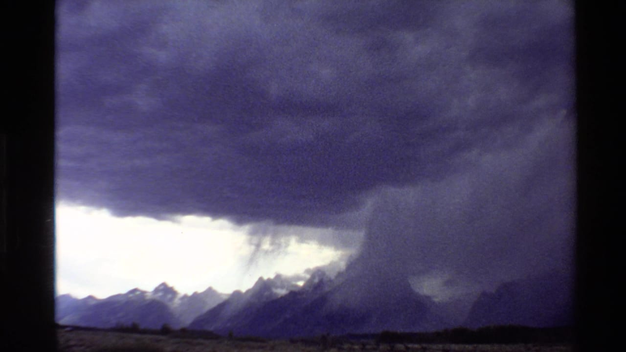 1980 8mm-style view from the Western United States showing dark clouds and rain falling over distant mountain peaks.