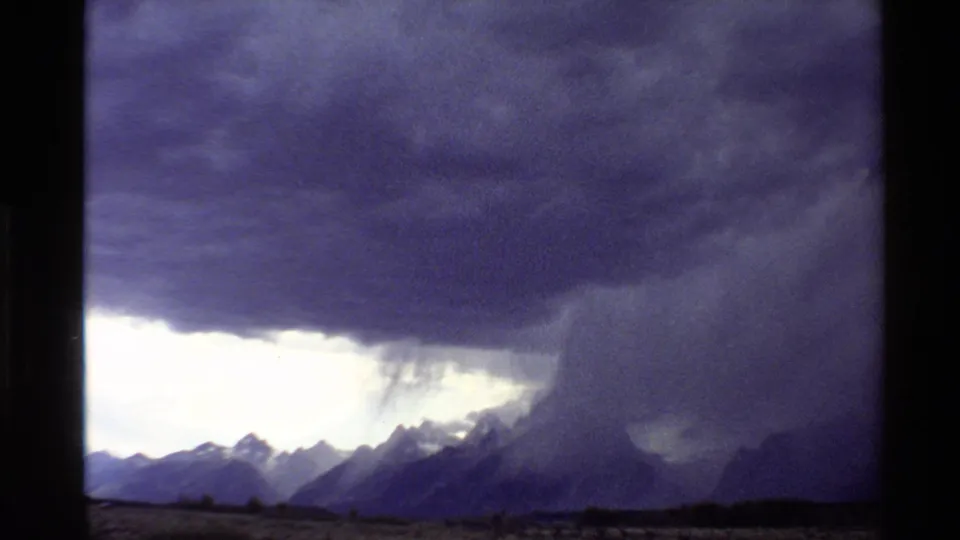 1980 8mm-style view from the Western United States showing dark clouds and rain falling over distant mountain peaks.