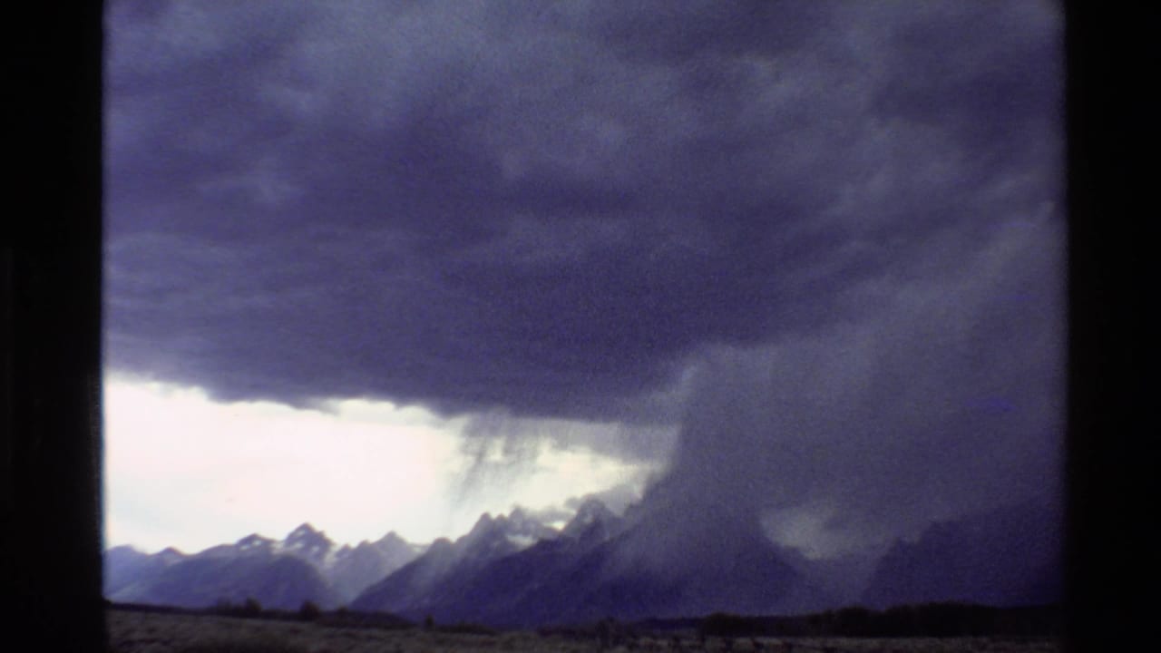 Western United States mountain landscape under a dark 1980 8mm storm front, with a visible rain shaft near the peaks.