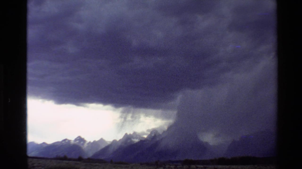 1980 Western U.S. 8mm frame showing a heavy grey storm cloud dropping rain over distant mountain ridges.