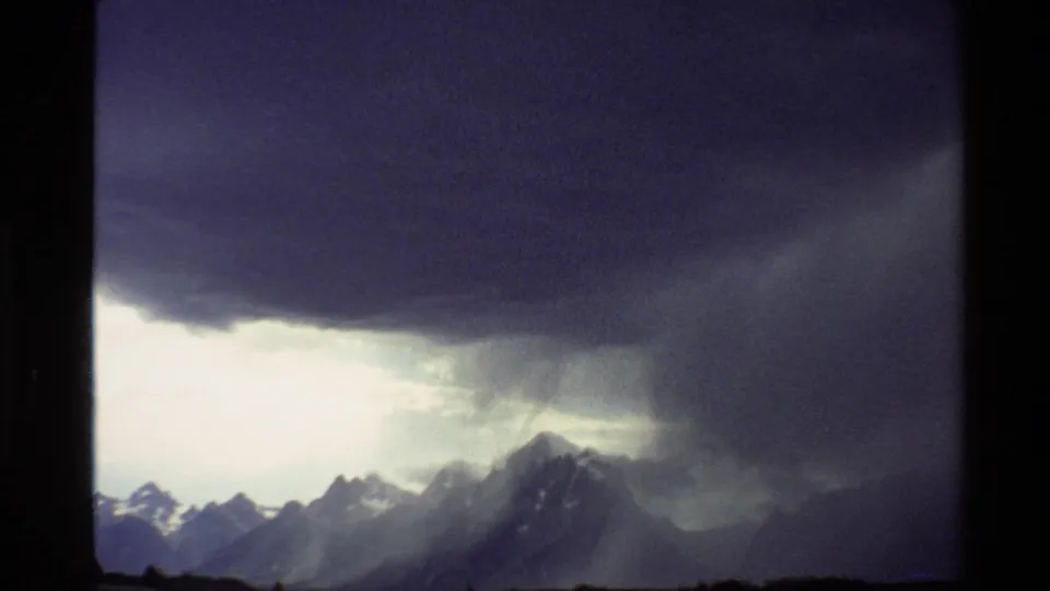 1980 Western U.S. 8mm frame with a broad grey storm cloud and visible rain falling over a mountain range.