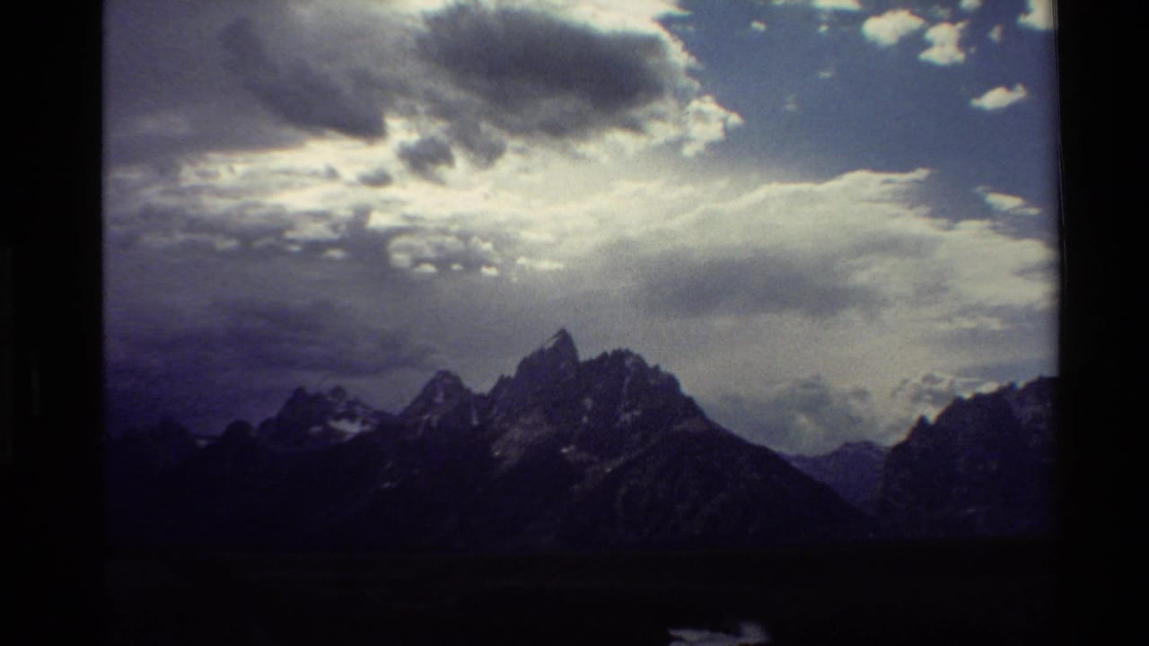1980 Western USA 8mm frame with sunlight filtering through clouds over jagged mountain peaks.