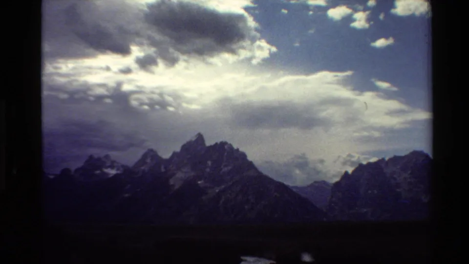 1980 Western USA 8mm frame showing a broad mountain ridge under layered clouds and blue sky.
