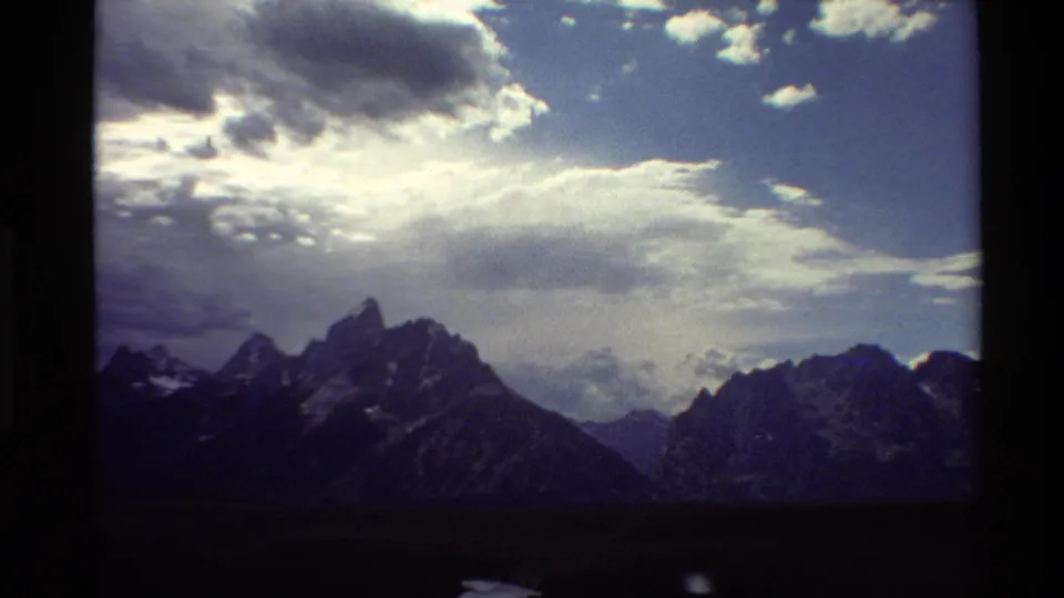 1980 Western USA 8mm frame of jagged mountain peaks beneath a bright, broken cloud deck.