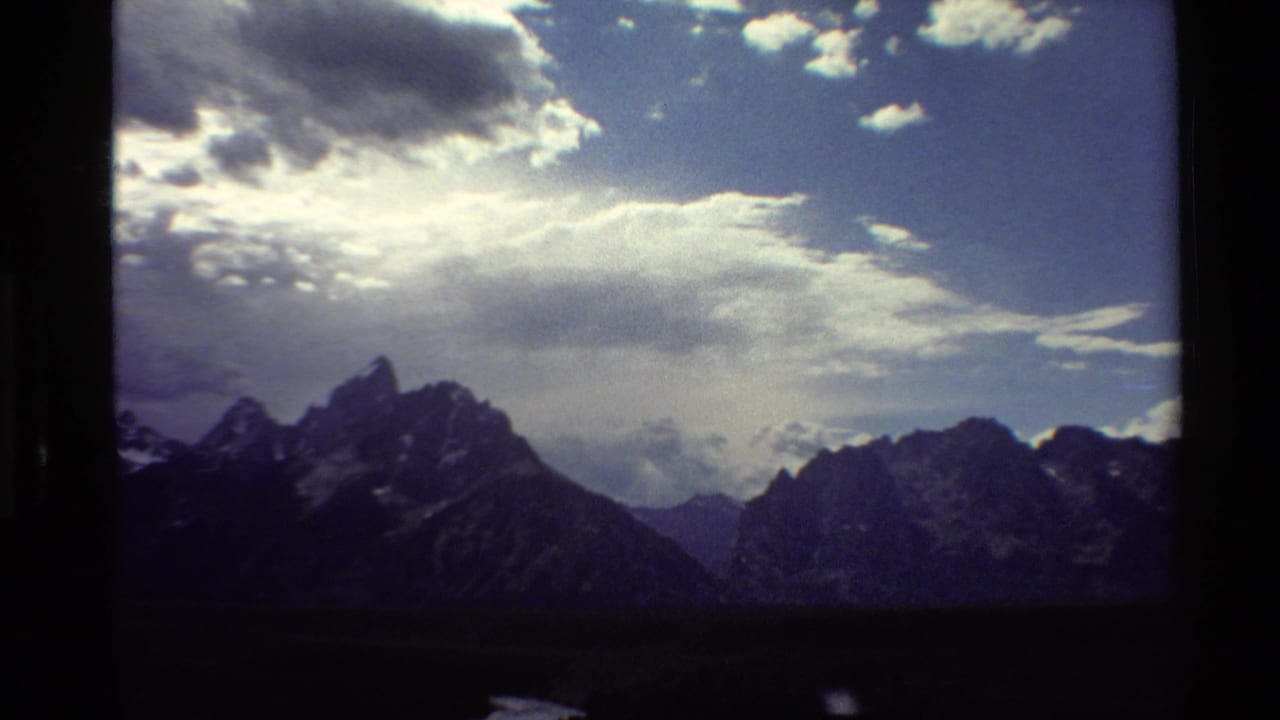 1980 8mm Western USA landscape frame showing rugged snow-dusted peaks under a dramatic cloudy sky.