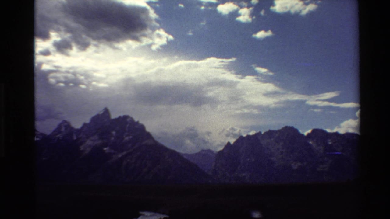 1980 8mm Western USA view of craggy mountains under sunlit clouds, with soft grain and vignetting.