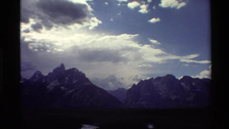 1980 8mm Western USA view of craggy mountains under sunlit clouds, with soft grain and vignetting.