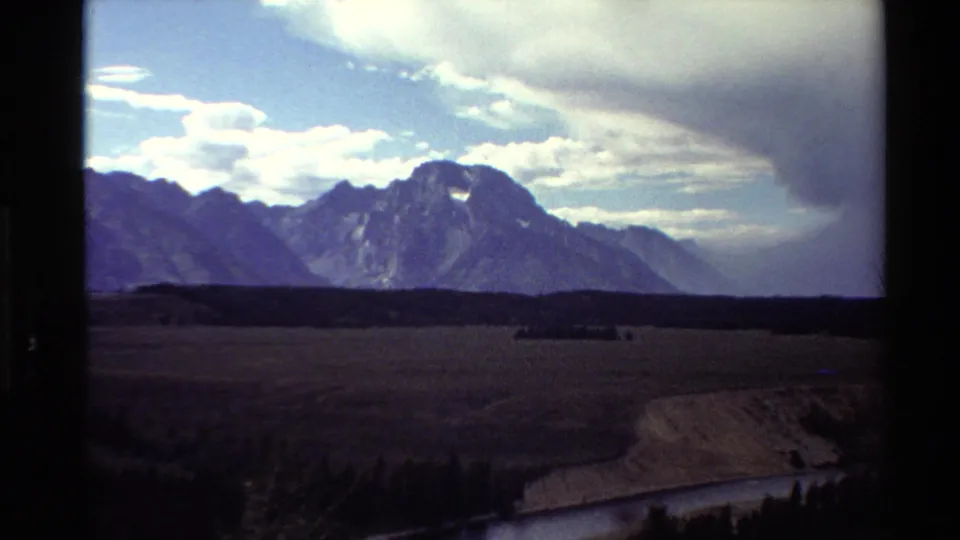 1980 8mm Western USA wide landscape with open plain, river bend, dark treeline, and distant mountains.