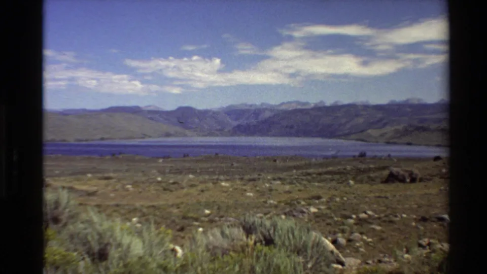 1980 8mm landscape frame showing an open Western U.S. plain, calm blue lake, distant slopes, and visible home-movie film borders.