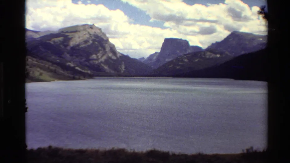 1980 Western U.S. 8mm frame showing a lake panorama, rugged mountain walls, a flat-topped peak, and scattered clouds.