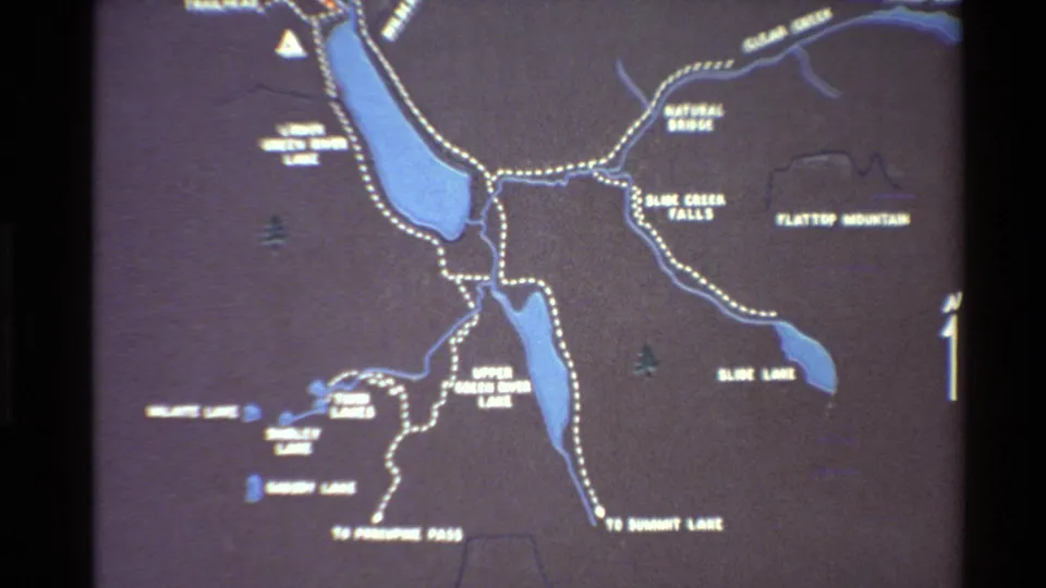 Wider 8mm view of the park map showing labeled lakes, trail routes, small symbols, and a compass arrow.