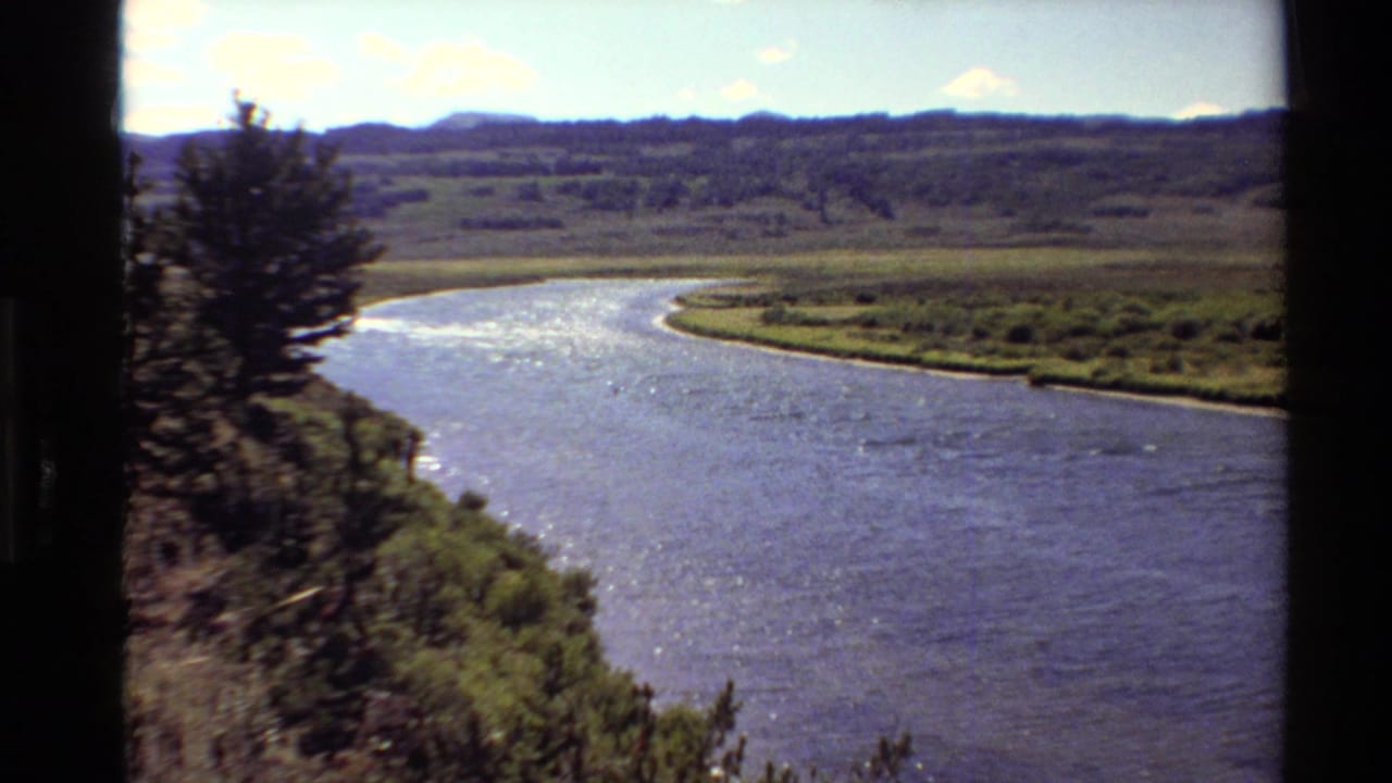 1980 Western USA 8mm view of a winding river, grassy banks, pine trees, and distant rolling terrain.