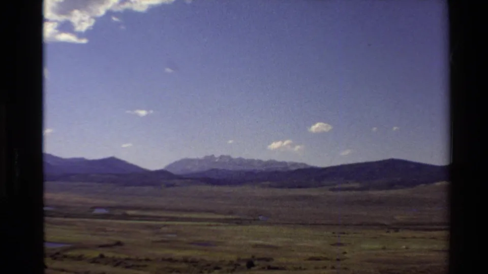 1980 Western USA 8mm landscape view of a broad plain, distant mountain range, and sparse clouds in a blue sky.