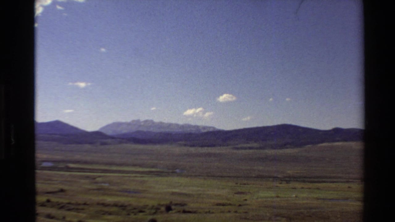 1980 Western U.S. 8mm frame showing a broad plain, distant mountain range, scattered clouds, and dark gate edges from the film scan.