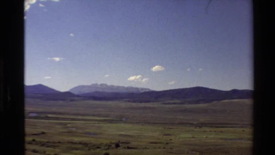 1980 Western U.S. 8mm frame showing a broad plain, distant mountain range, scattered clouds, and dark gate edges from the film scan.