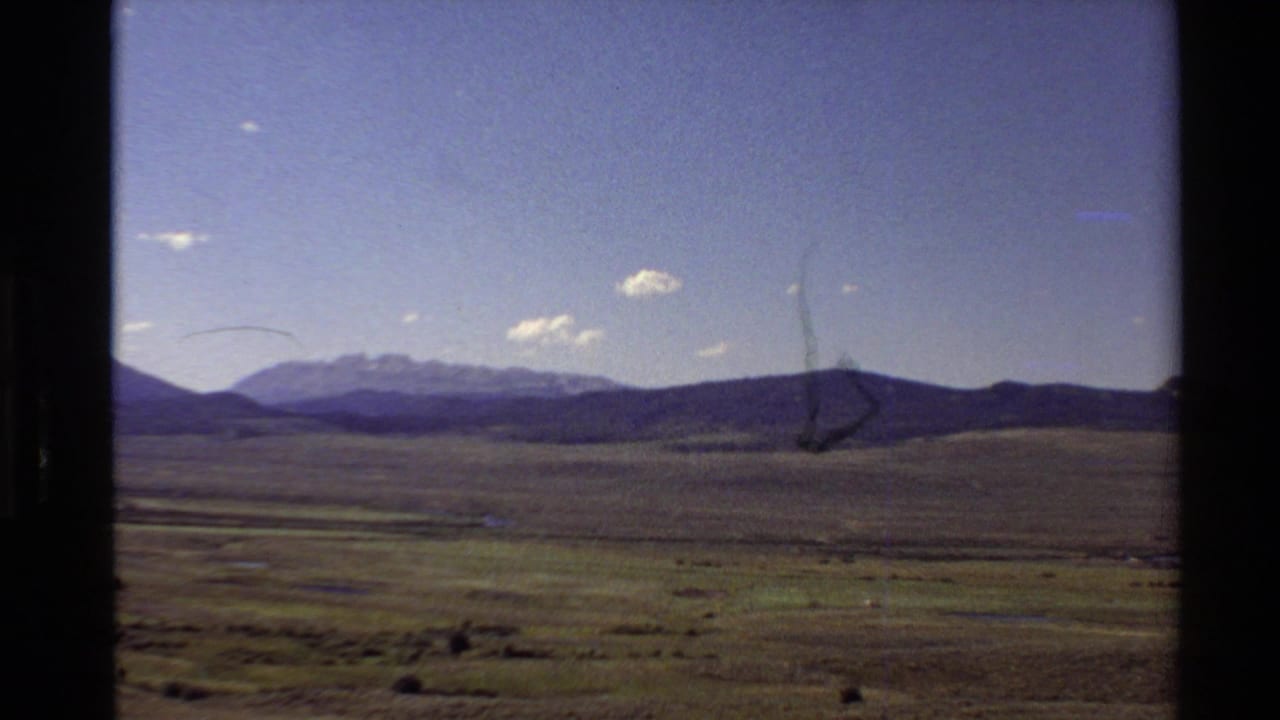 Wide valley landscape with low hills, distant mountains, and visible film scratches.