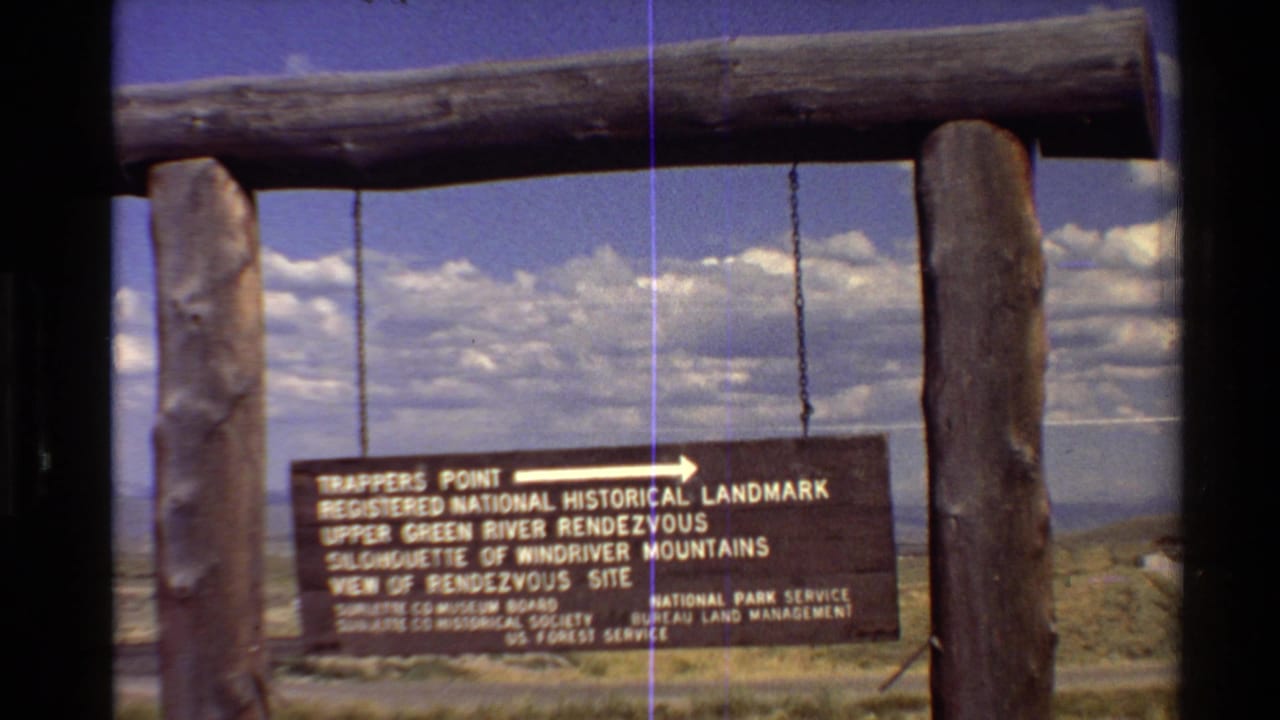 1980 8mm frame of a Trappers Point landmark sign suspended from a rustic log structure in the Western U.S. landscape.