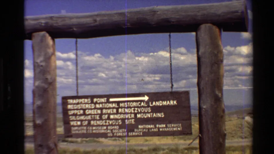 A wide 8mm view shows the historic landmark sign beneath a log crossbeam, with the Western U.S. landscape in the background.