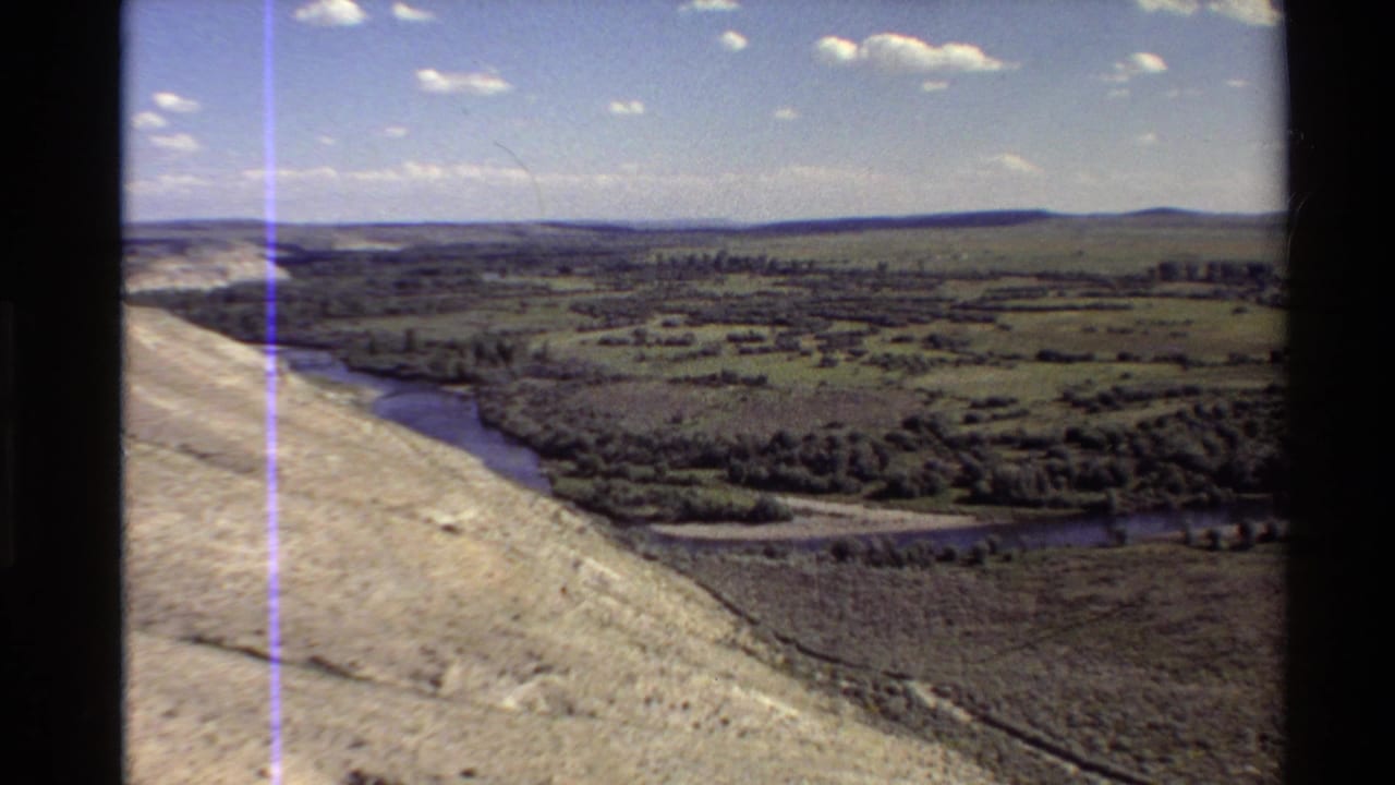 River valley and rolling fields seen from above, with a pale slope at left and clouds overhead.