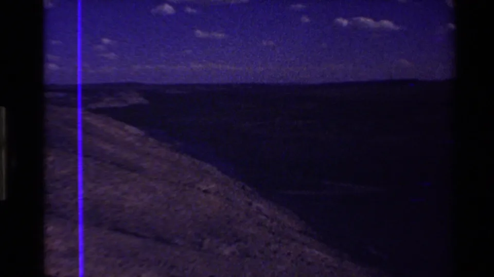 Blue-toned 8mm aerial frame of a hillside and distant ridge in the Western U.S., with heavy underexposure and a vertical purple film line.