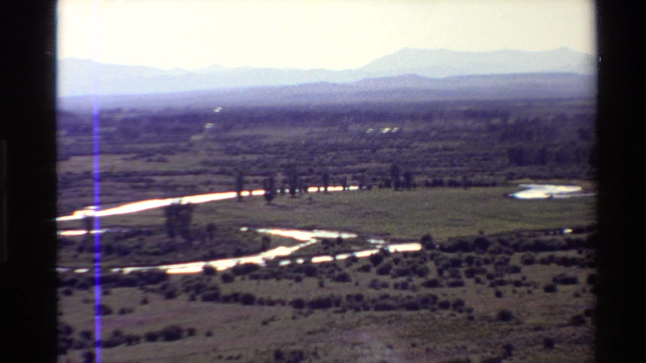 1980s 8mm Western U.S. landscape view of a reflective winding river crossing grassy plains beneath hazy mountains.