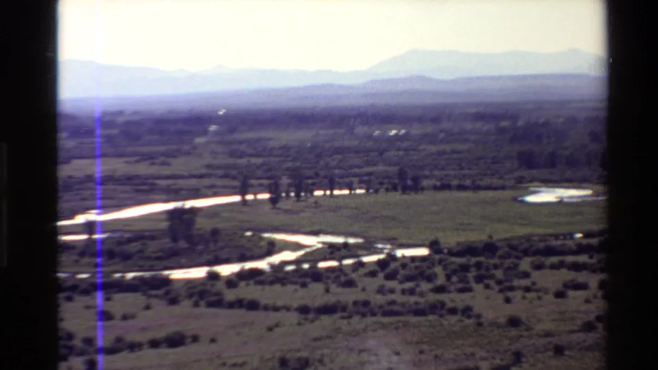 1980s 8mm Western U.S. landscape view of a reflective winding river crossing grassy plains beneath hazy mountains.