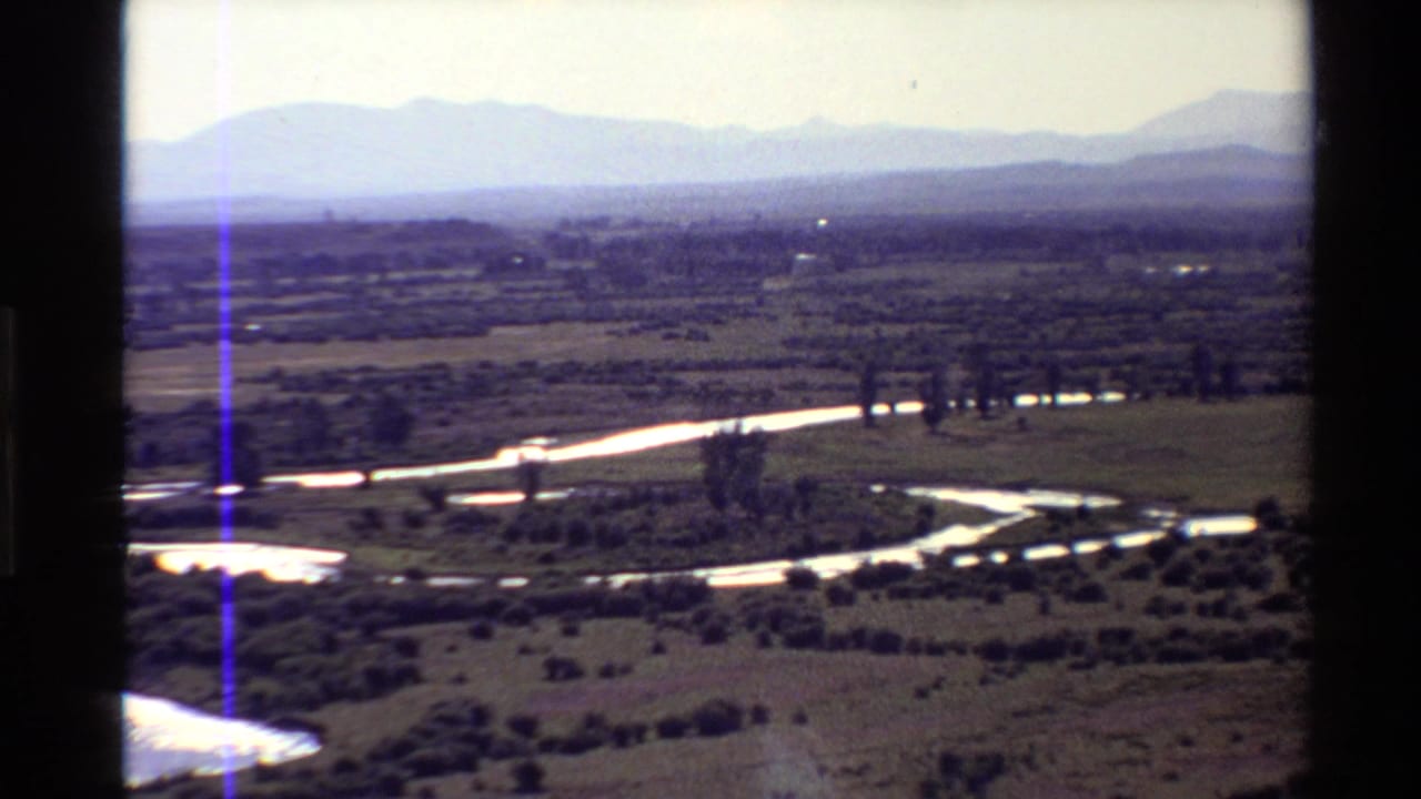 Reflective river bends through open plains with mountains on the horizon.