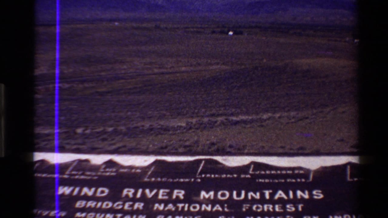 1980 8mm frame of a Western U.S. plain and distant ridge, with partial Wind River Mountains Bridger National Forest sign visible in front.