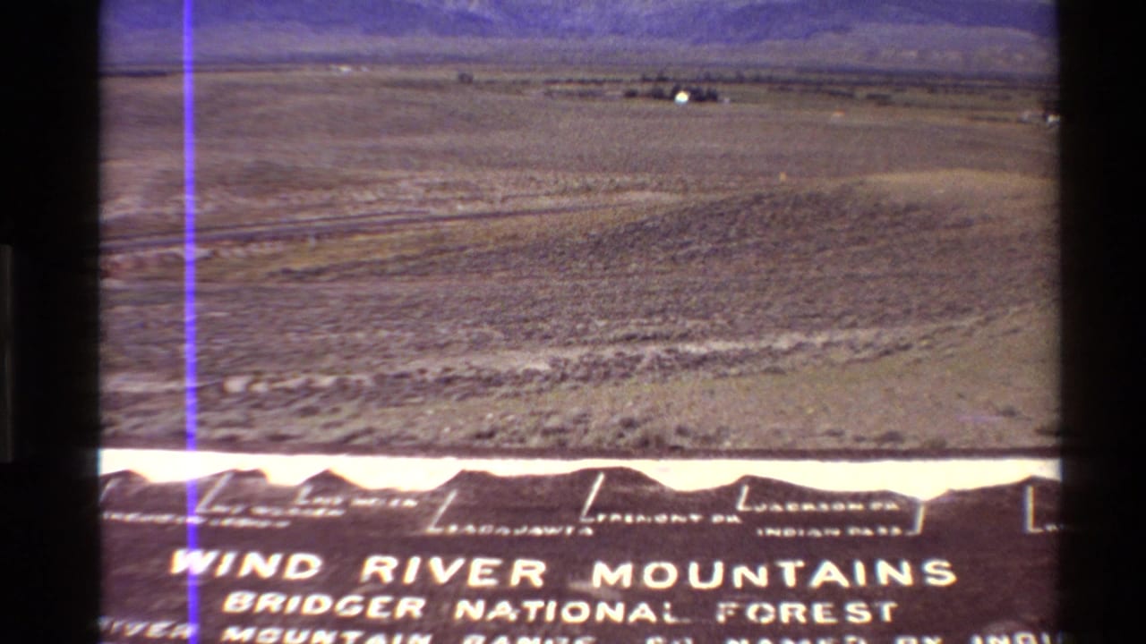 Open plain and distant ridge above a foreground sign reading Wind River Mountains Bridger National Forest.