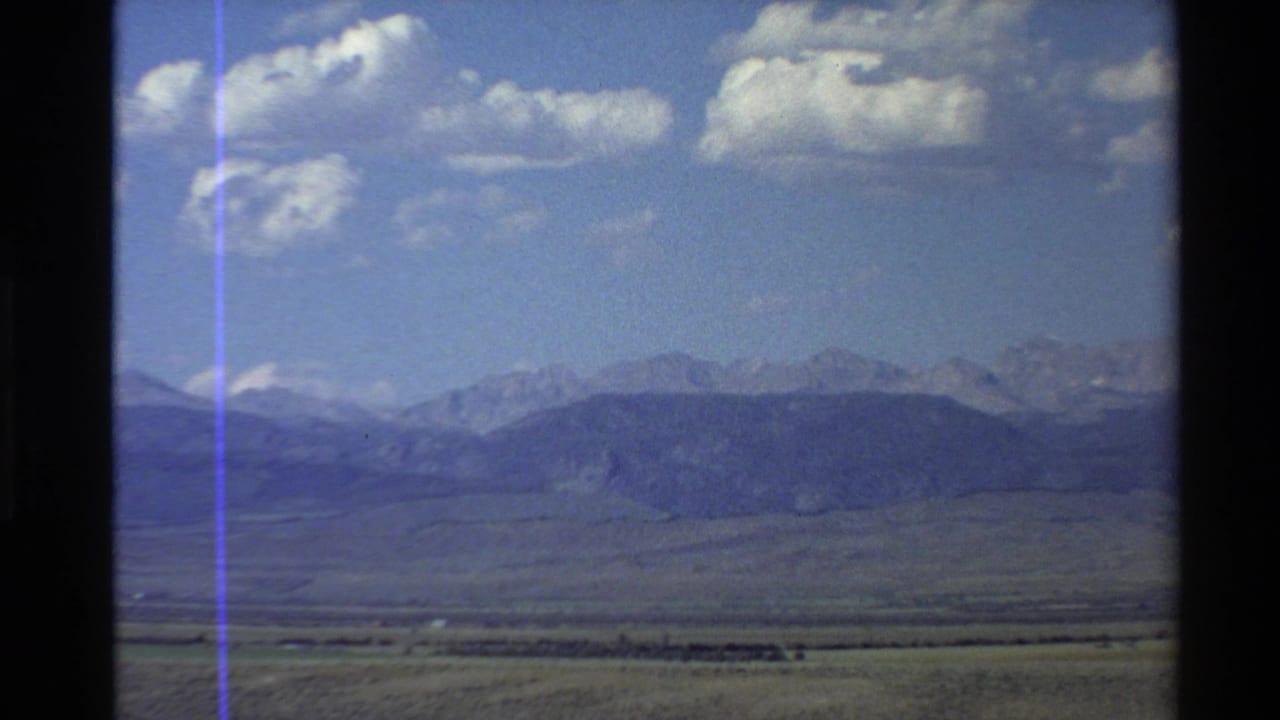 Wide valley landscape with distant mountain range under scattered clouds.