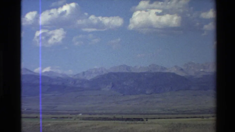 1980 8mm Western U.S. valley panorama with distant mountains, blue sky, and scattered white clouds.