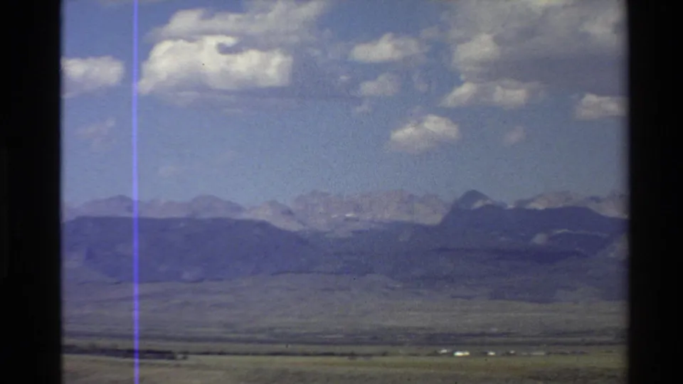 1980 Western U.S. 8mm frame showing a flat valley foreground, distant mountain range, clouds, and visible film artifacts.