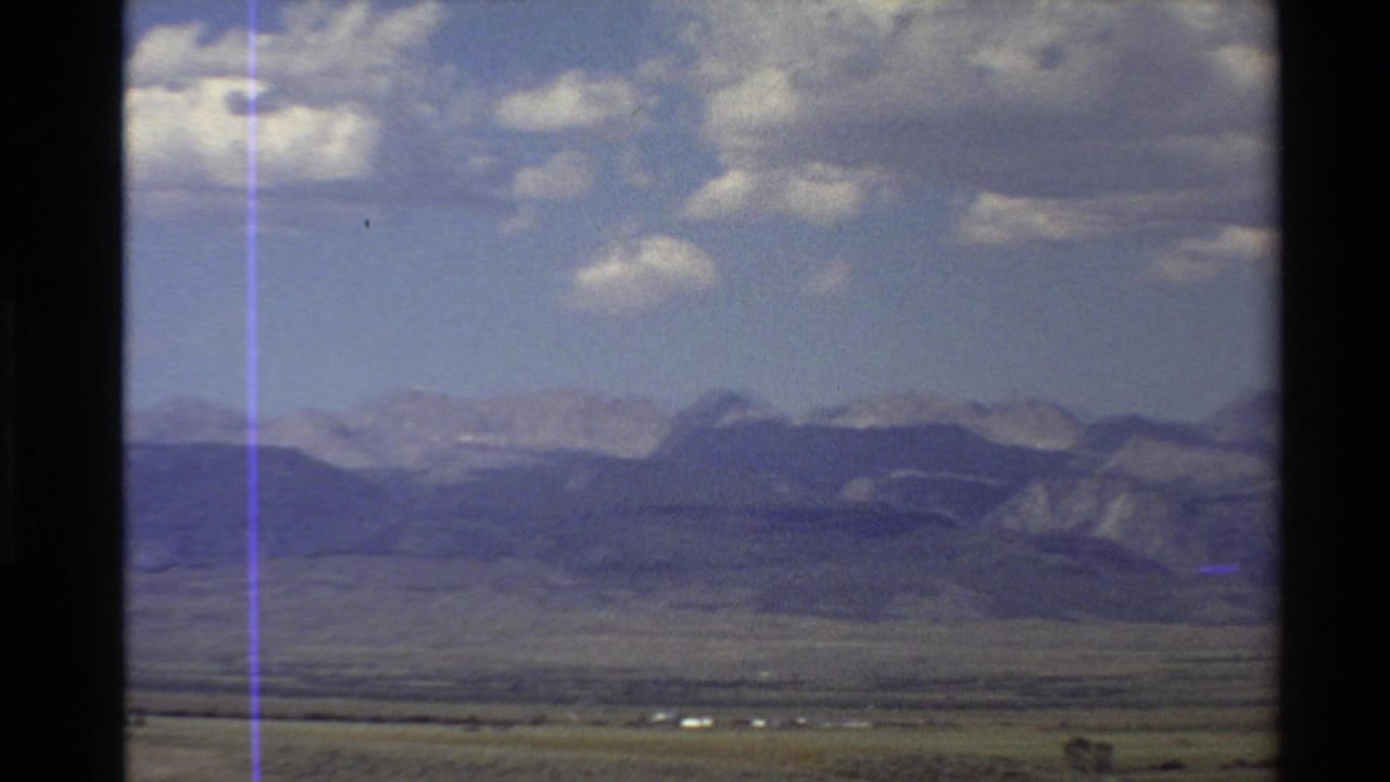 Western USA landscape view with open desert, distant mountain ridges, scattered clouds, and a dark vertical divider in the foreground.