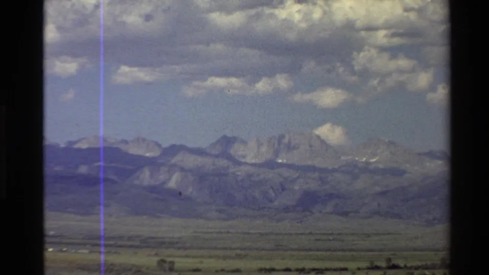 1980 Western USA frame showing ridged mountains, a broad desert floor, broken clouds, and dark window or film-frame borders.