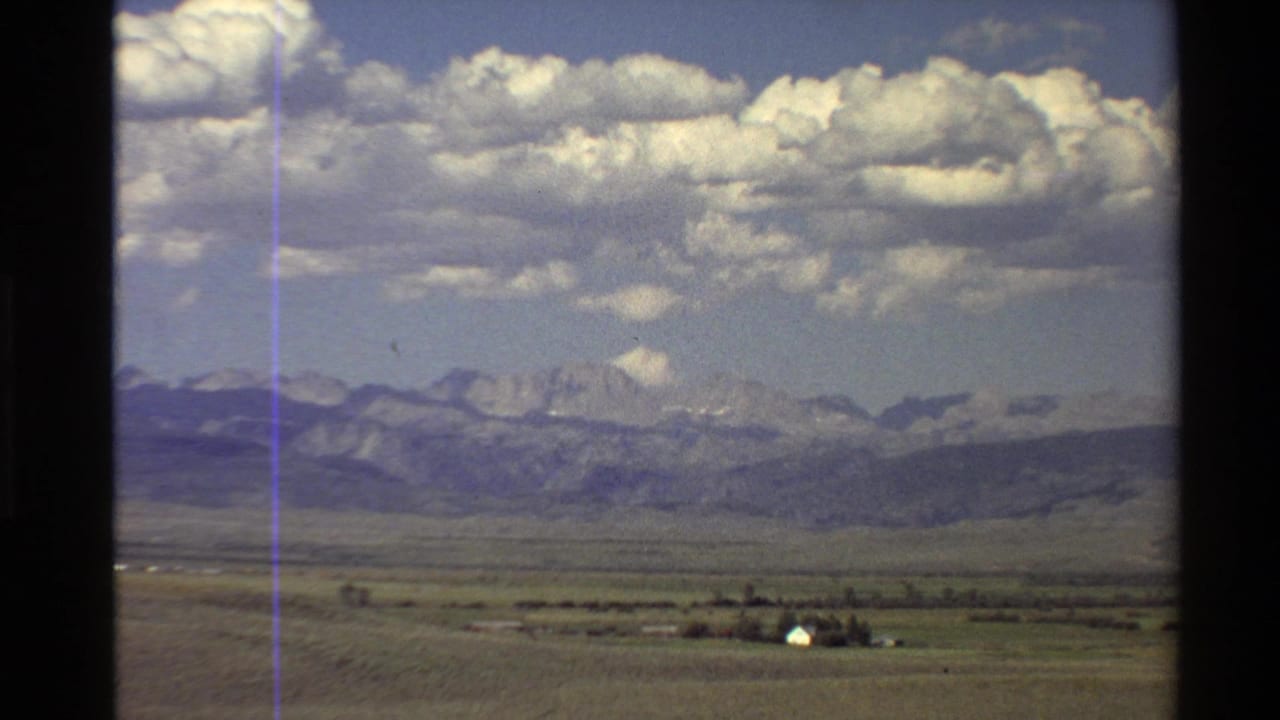 Mountain range, open plain, clouds, and a small white house in the foreground.