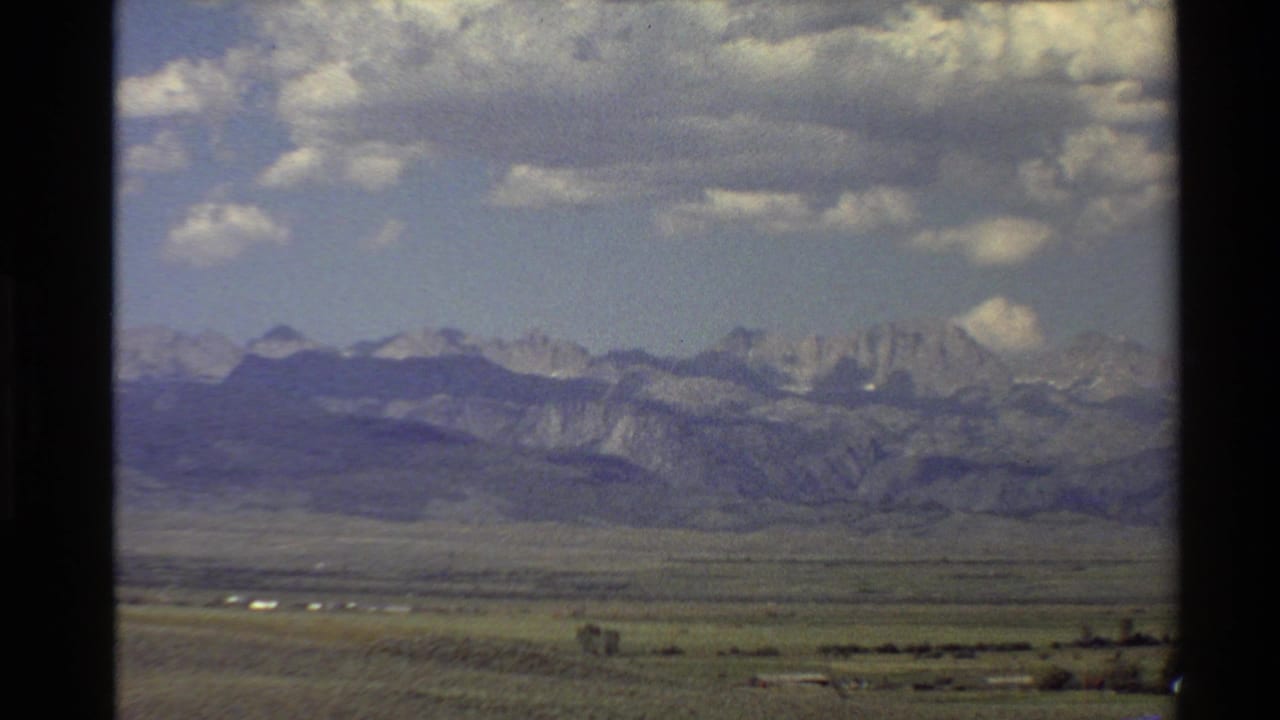 1980 Western U.S. home-movie view of a broad valley leading to distant rugged mountains beneath scattered clouds.