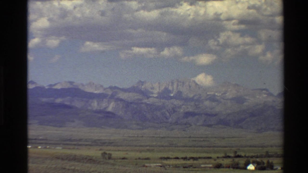 Mountain range and valley landscape with clouds overhead and a small pale building near the lower right.
