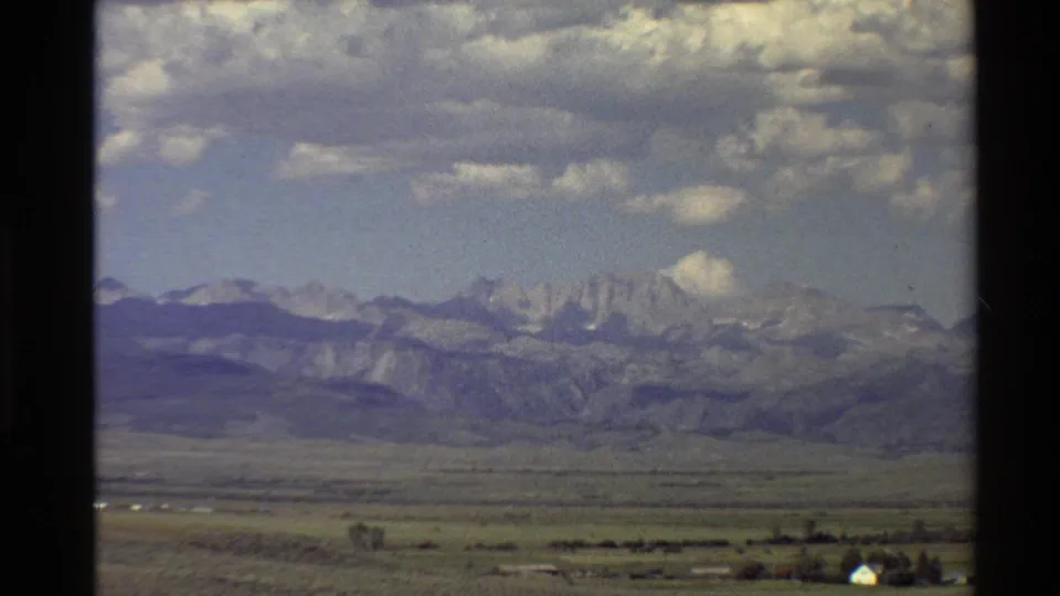 1980 Western U.S. landscape view showing distant mountains, open valley ground, cloudy sky, and a small pale structure.