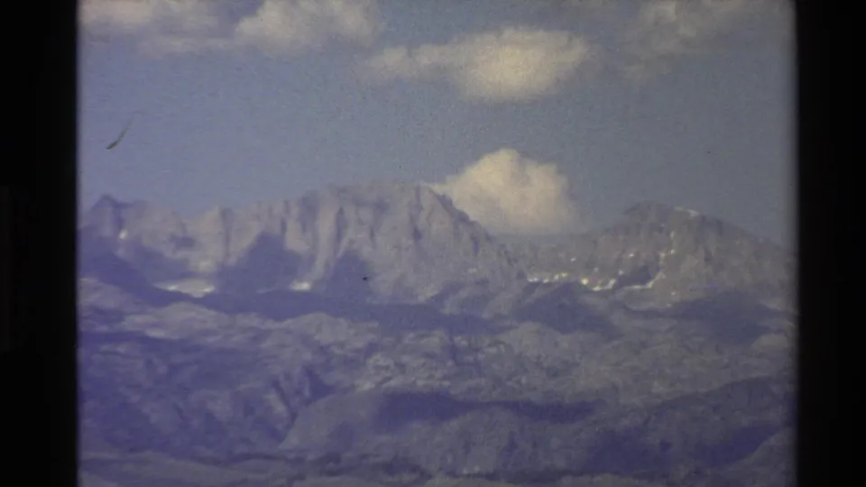 Soft, grainy 1980 Western U.S. mountain view with rugged peaks, lower ridges, and clouds framed by dark borders.