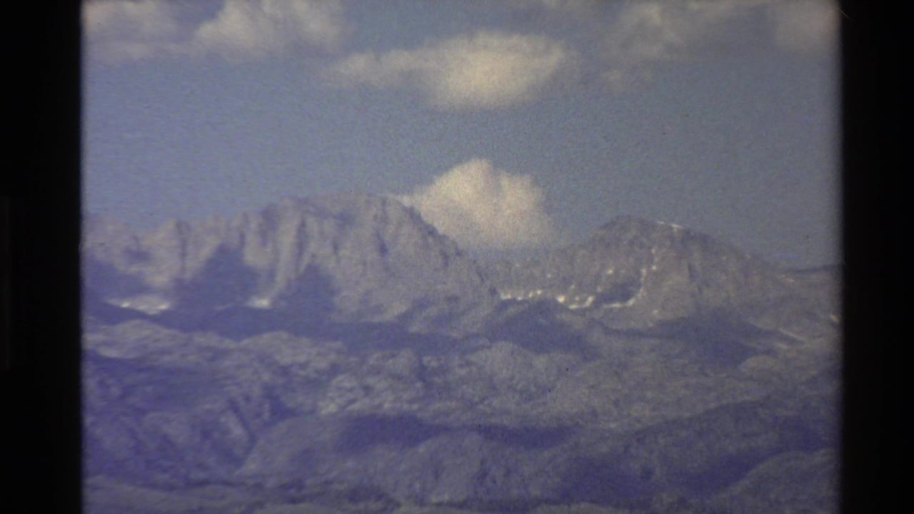 Western U.S. 1980 8mm view of rugged mountain peaks with light cloud cover and soft archival color.
