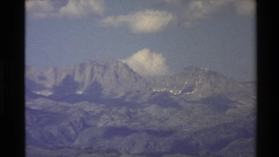 Western U.S. 1980 8mm view of rugged mountain peaks with light cloud cover and soft archival color.