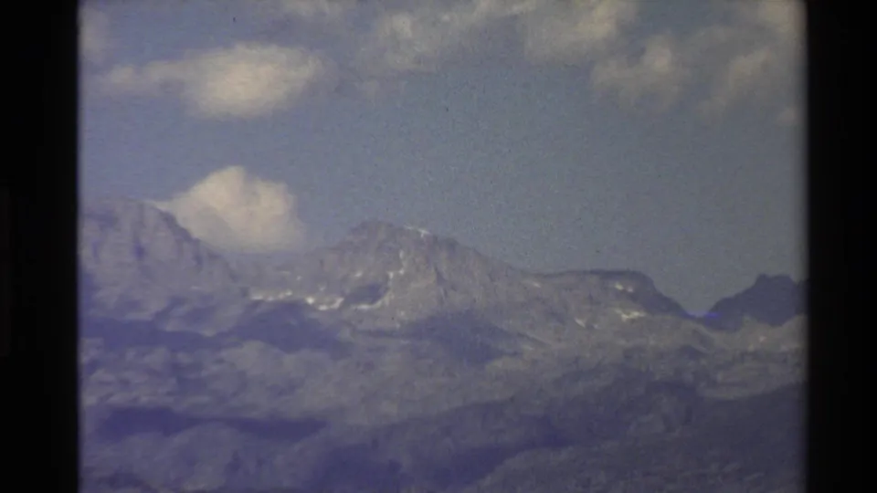 Western U.S. 1980 8mm frame showing a hazy mountain ridge, scattered clouds, and visible home-movie film texture.