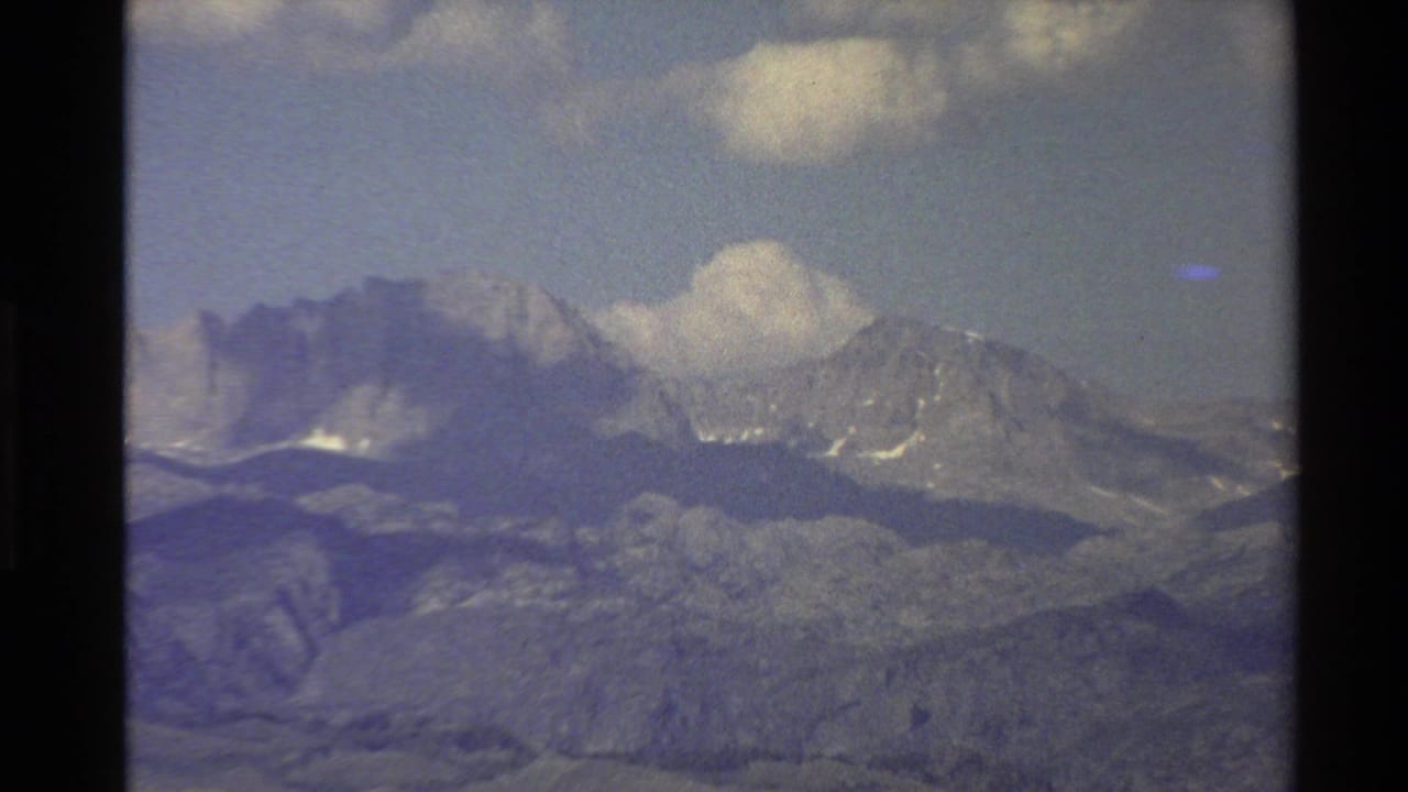 1980 Western U.S. 8mm view of a distant mountain range with snow patches, layered hills, and clouds above.