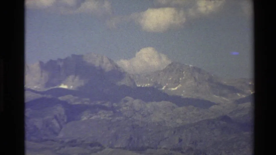 1980 Western U.S. 8mm view of a distant mountain range with snow patches, layered hills, and clouds above.