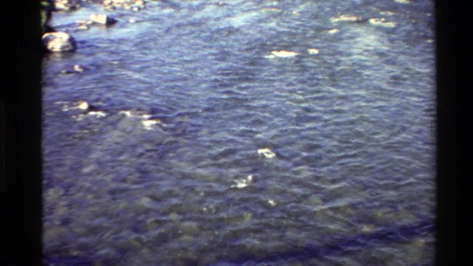 Final 1980s 8mm frame of the Western USA river pan, showing textured blue water, rocks, and bright ripples with visible film edges.