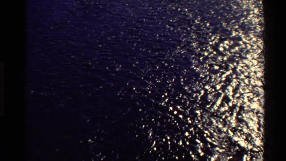 Blue-tinted 8mm frame of rippling water with strong sun glints and no visible people or structures.