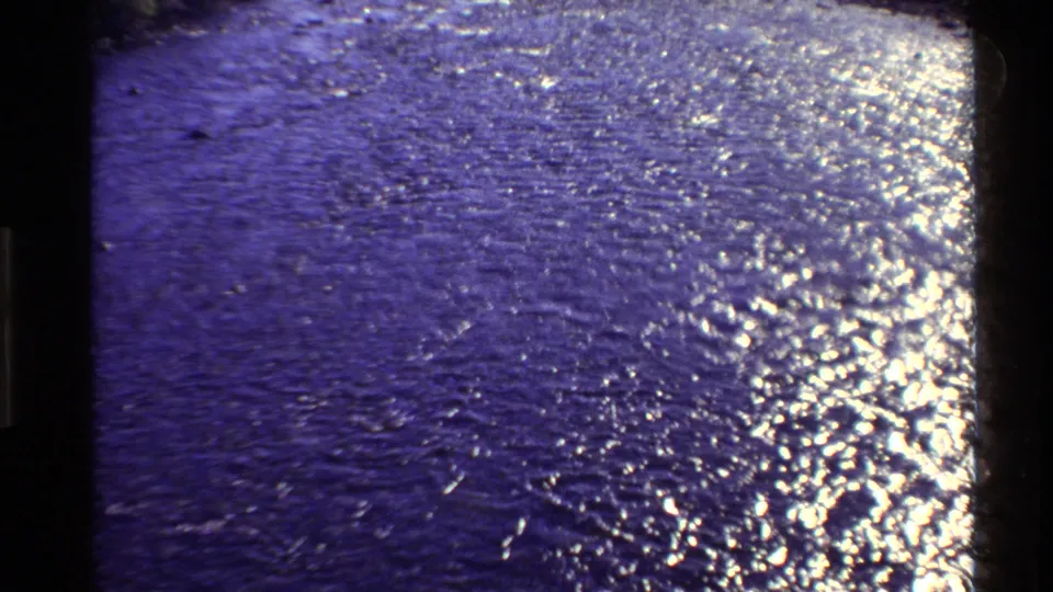 Final 8mm frame of rippling water in Western USA footage, with strong glare, grain, and purple-blue color shift.