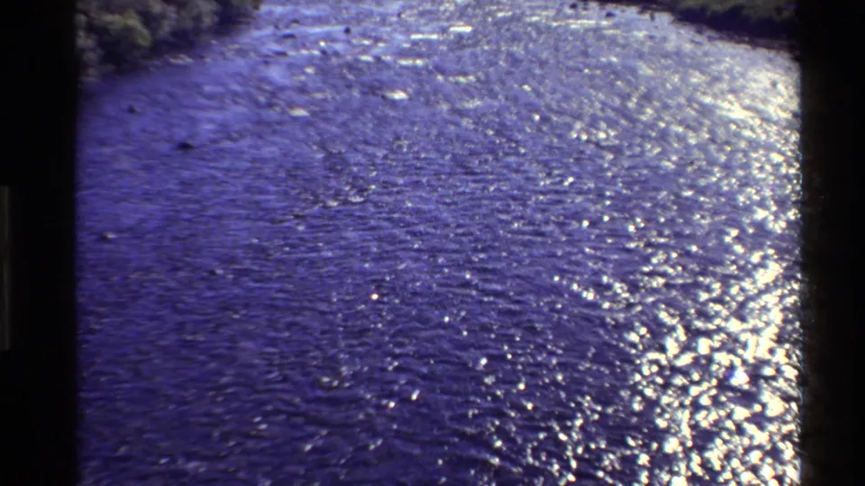1980 Western U.S. 8mm frame showing a broad river surface shimmering in wind, with low banks and distant hills beyond.