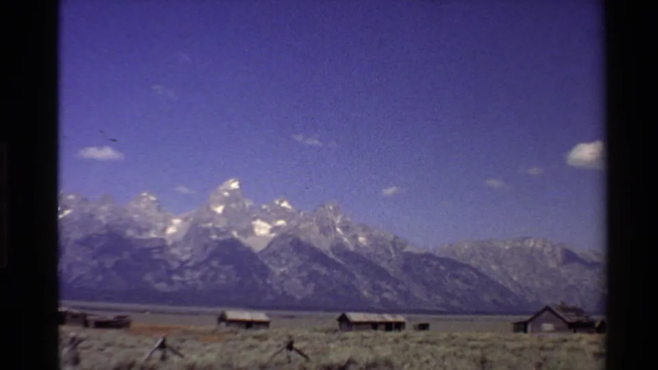 1980 Western U.S. 8mm view of a broad mountain range with rustic cabins and fence posts across a dry plain.